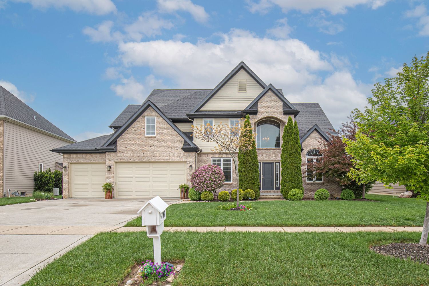 Modern suburban homes with well-maintained lawns and landscaping line a residential street on a sunny day.