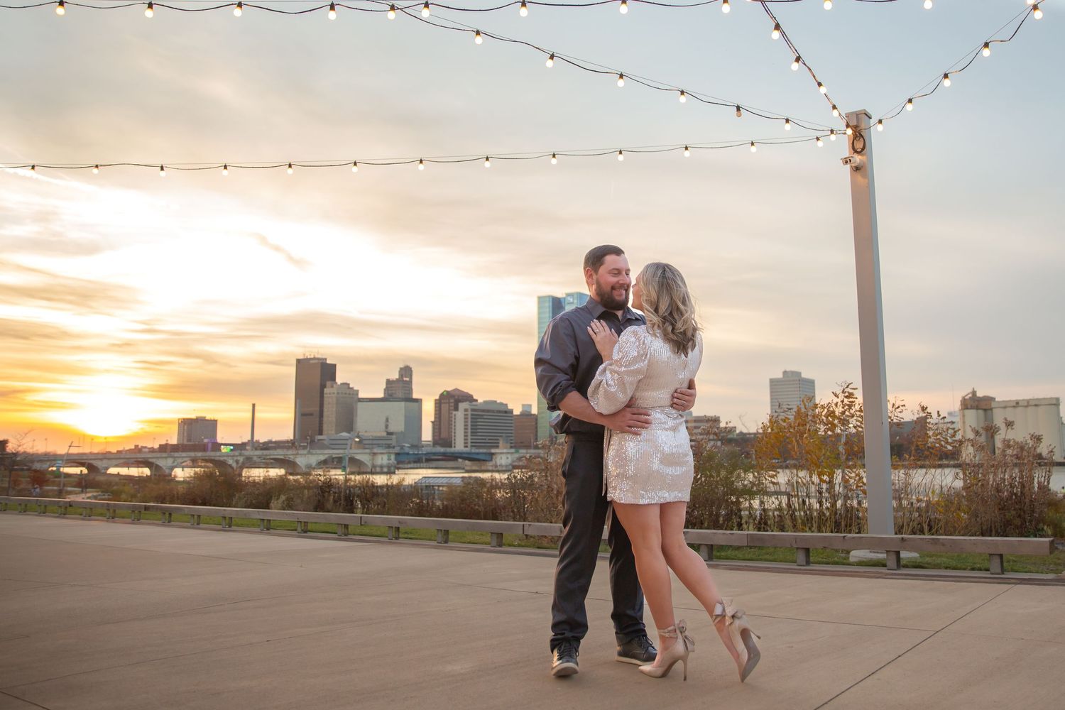 Couple dancing  with city skyline and string lights at sunset.