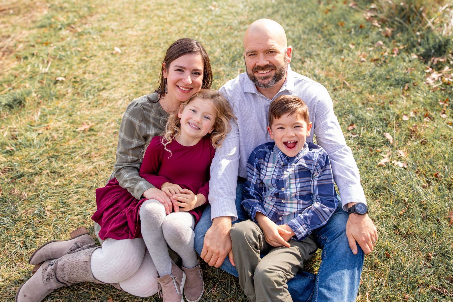 Family sitting together outdoors on grass during golden hour photography session.