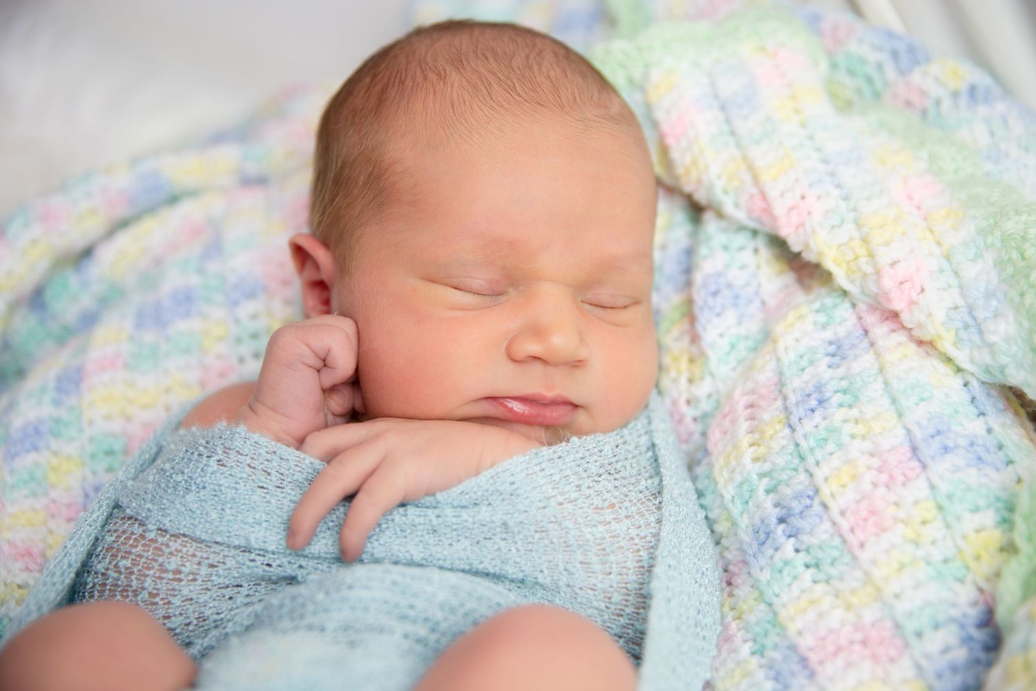 Peaceful newborn baby sleeping under a soft blue and pastel patterned blanket.