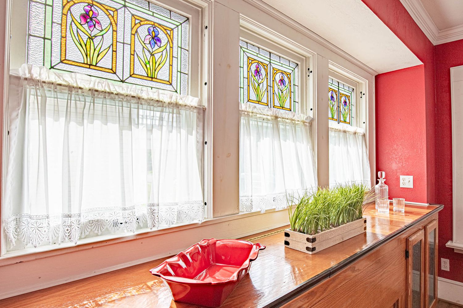 A bright interior hallway with stained glass windows, red accent walls, and white trim details along the ceiling.