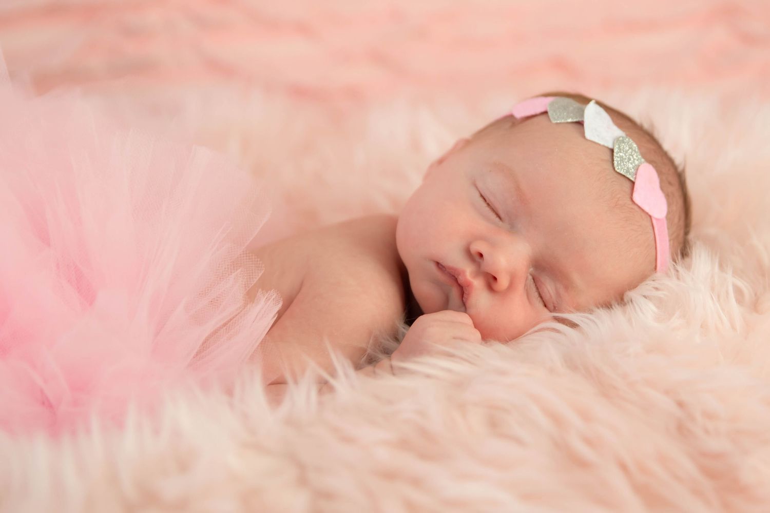 Sleeping baby on pink fur blanket wearing delicate headband.