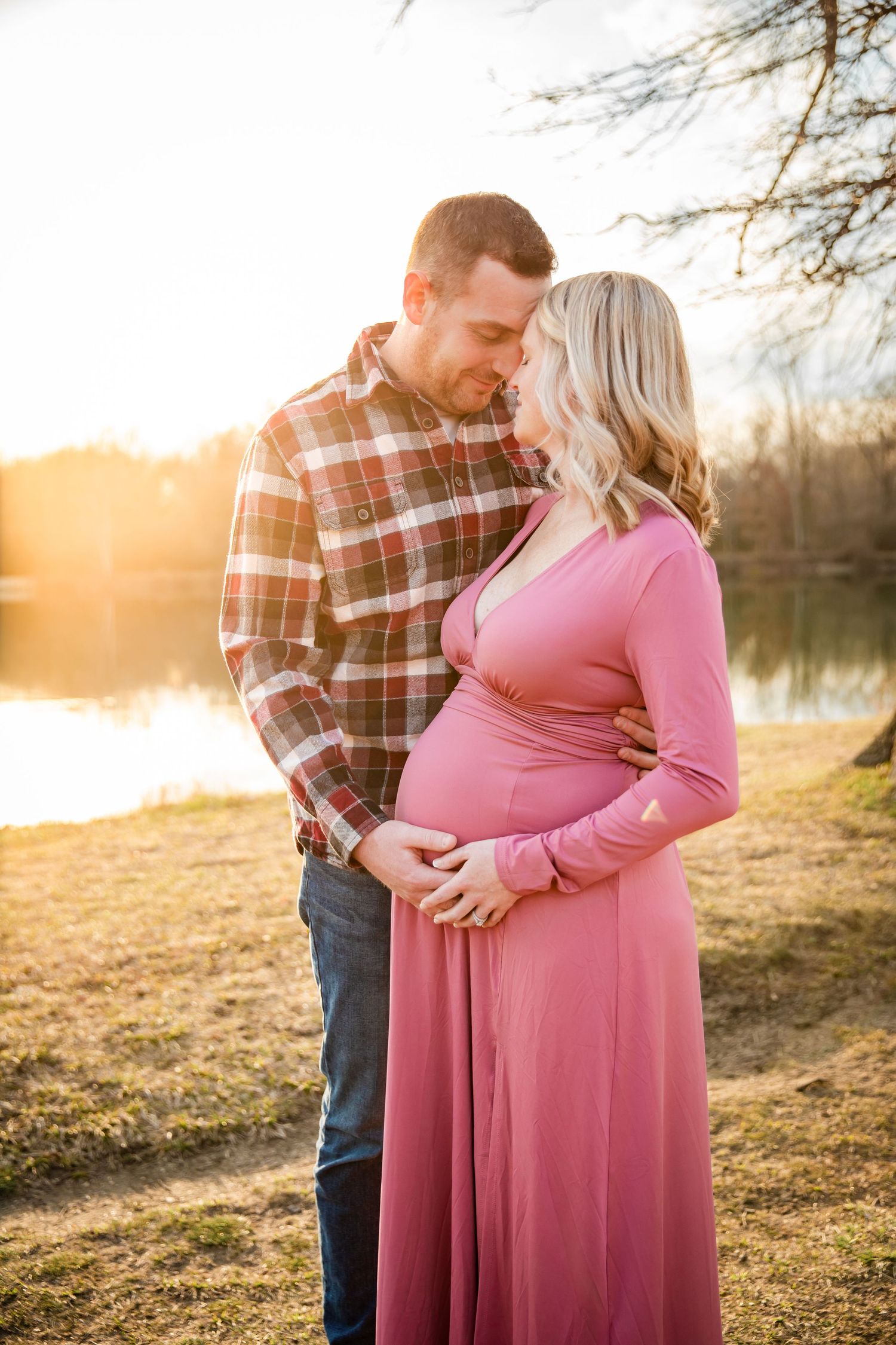 Romantic maternity photos at sunset with couple in pink dress and plaid shirt.