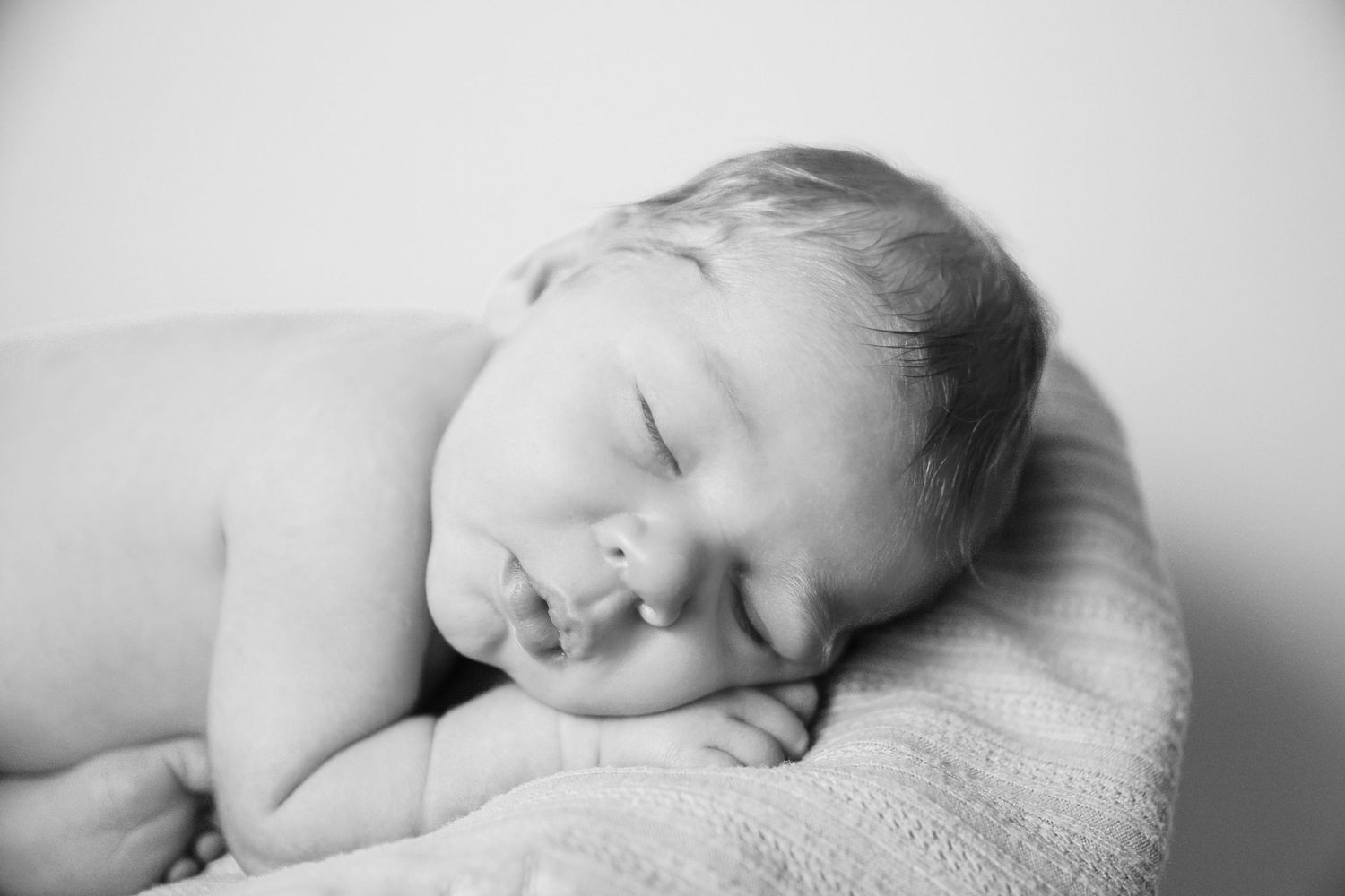 Serene black and white image of a sleeping newborn on soft blanket.
