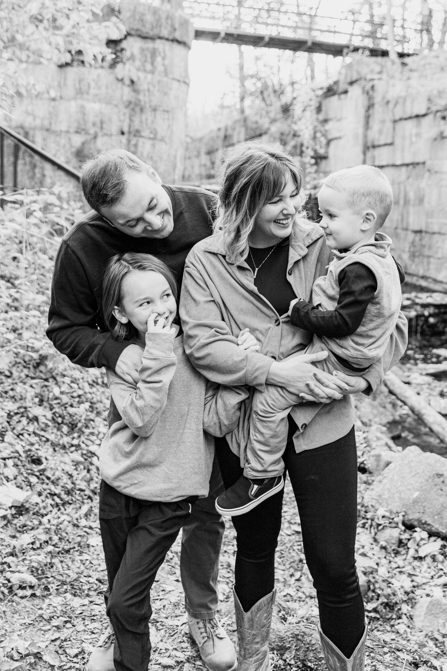 Black and white candid shots of playful family moments outdoors against stone wall.