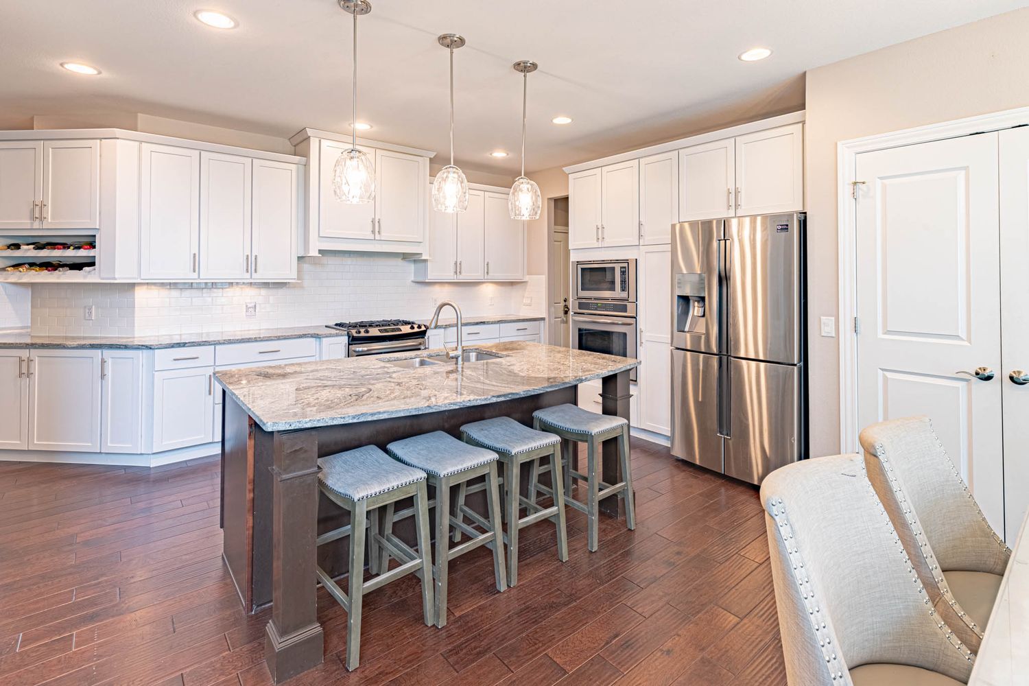 White kitchen with island seating, pendant lights, and modern bar stools.