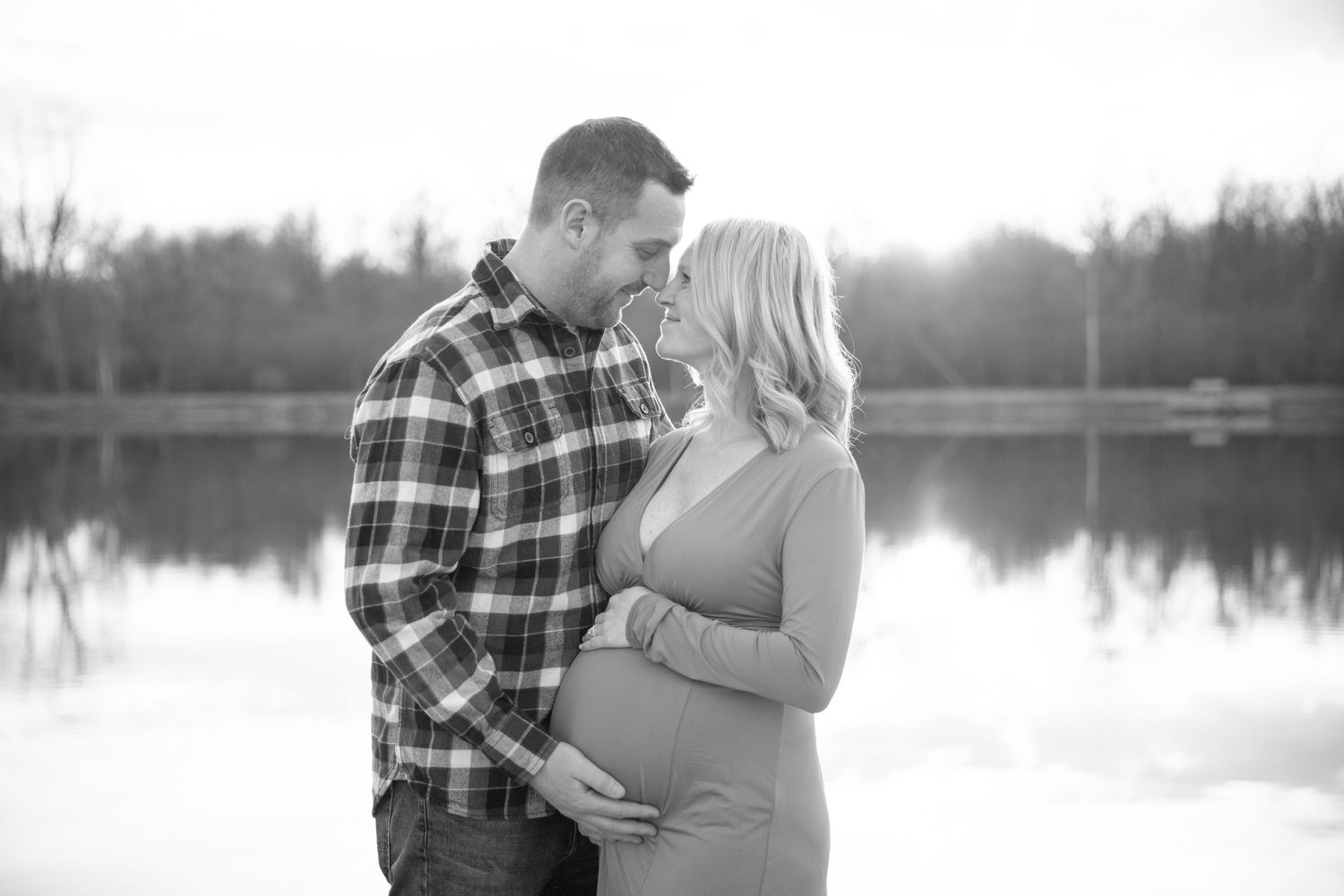 Romantic couple's maternity photoshoot by a serene lake at sunset.