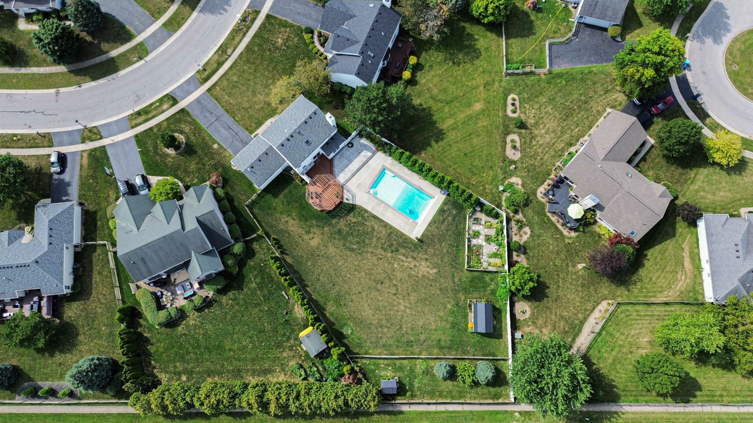 Drone view of suburban homes with curved streets and well-maintained lawns.