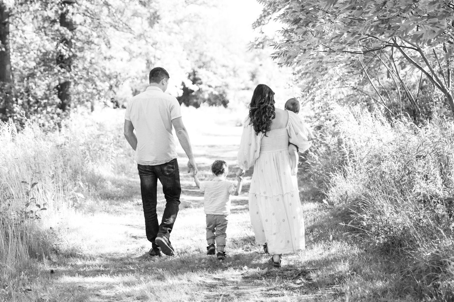 Black and white photo of a family walking together hand in hand down a nature path surrounded by foliage.