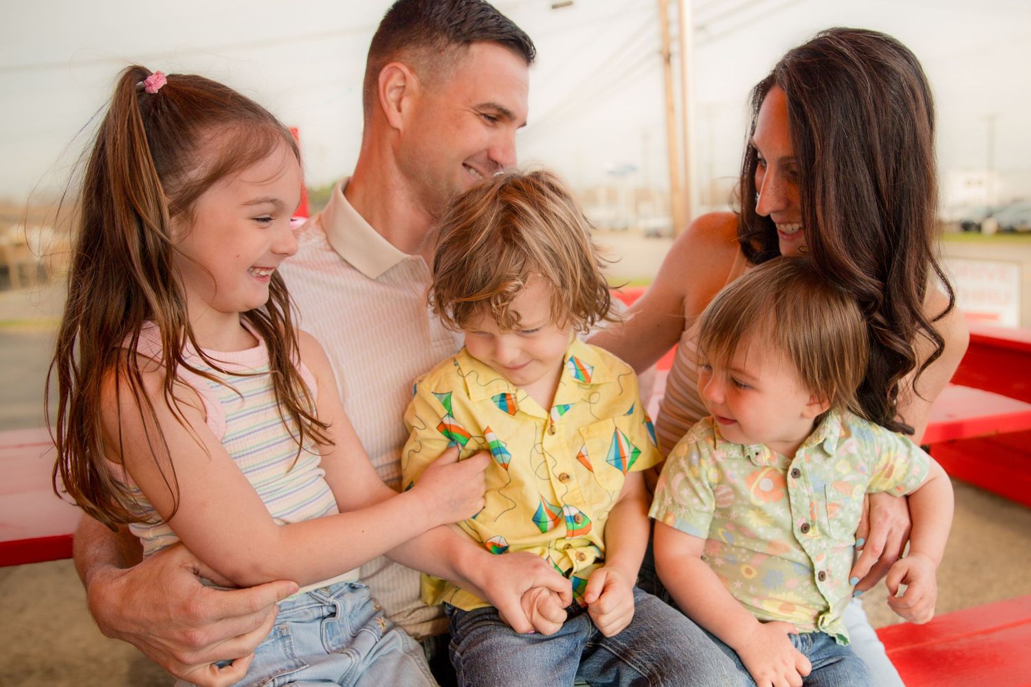 Happy family of five smiling together outdoors, parents with three young children in colorful summer outfits.