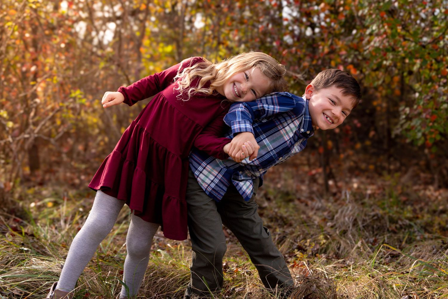 Family enjoying playful moments together in a fall forest setting with warm autumn colors.
