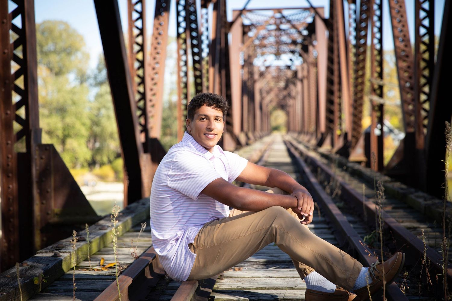 Person in white shirt sits on rustic railroad bridge tracks.