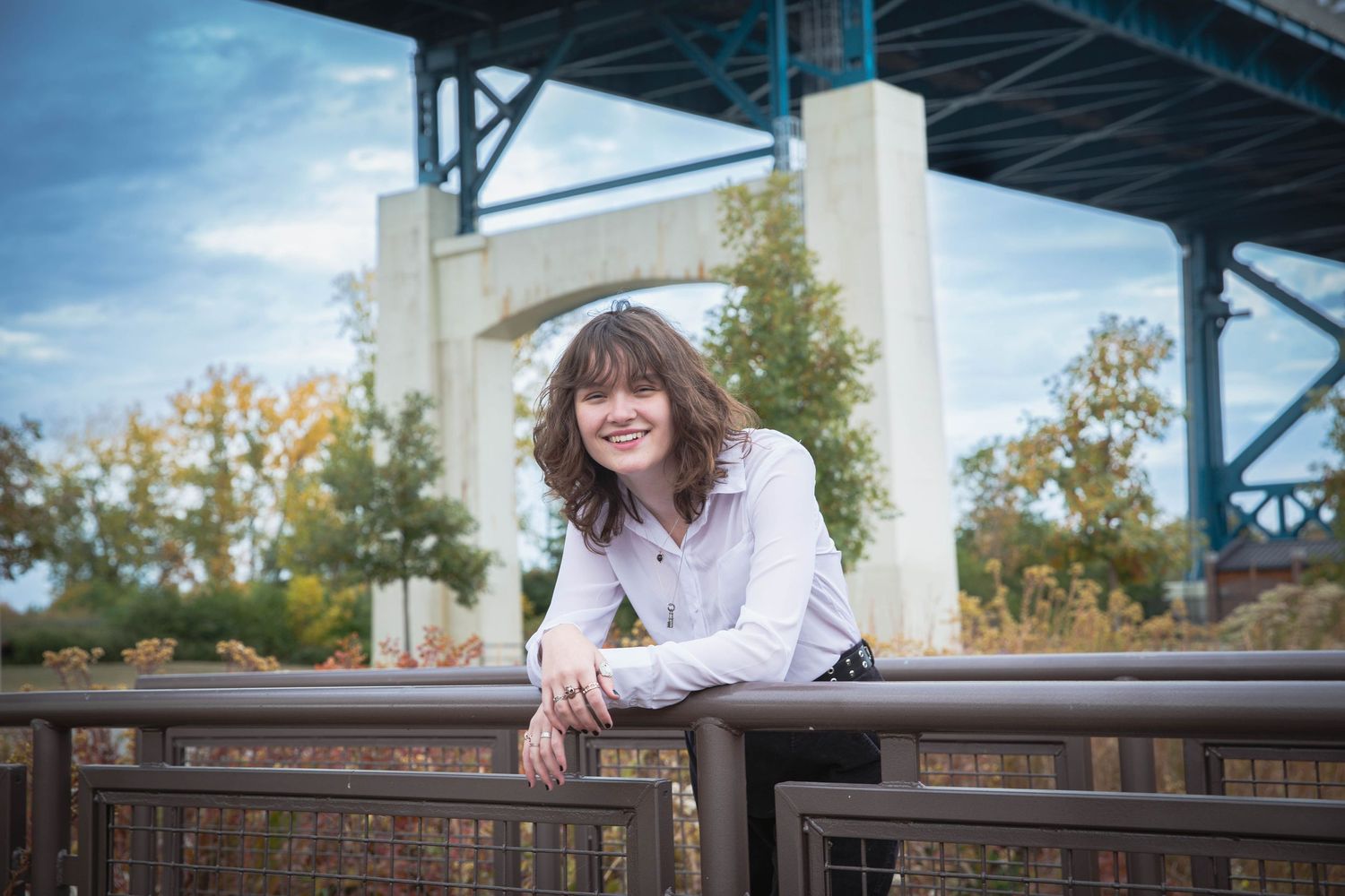 Portrait of person leaning on railing under bridge structure.