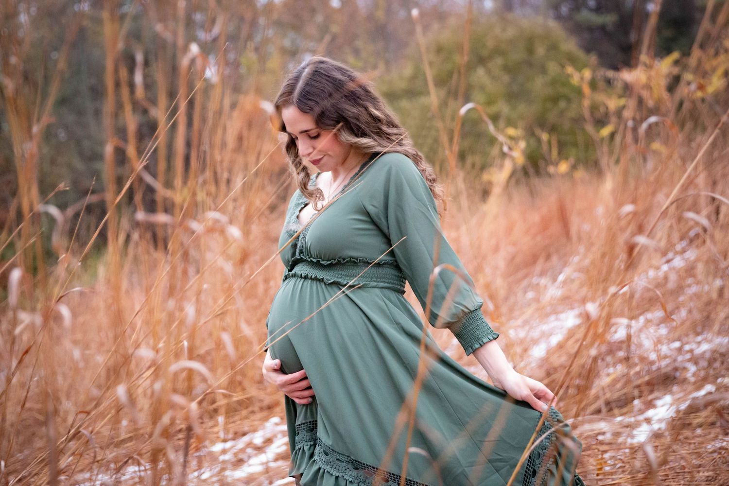 Person in green sweater poses against autumn foliage during outdoor maternity session.