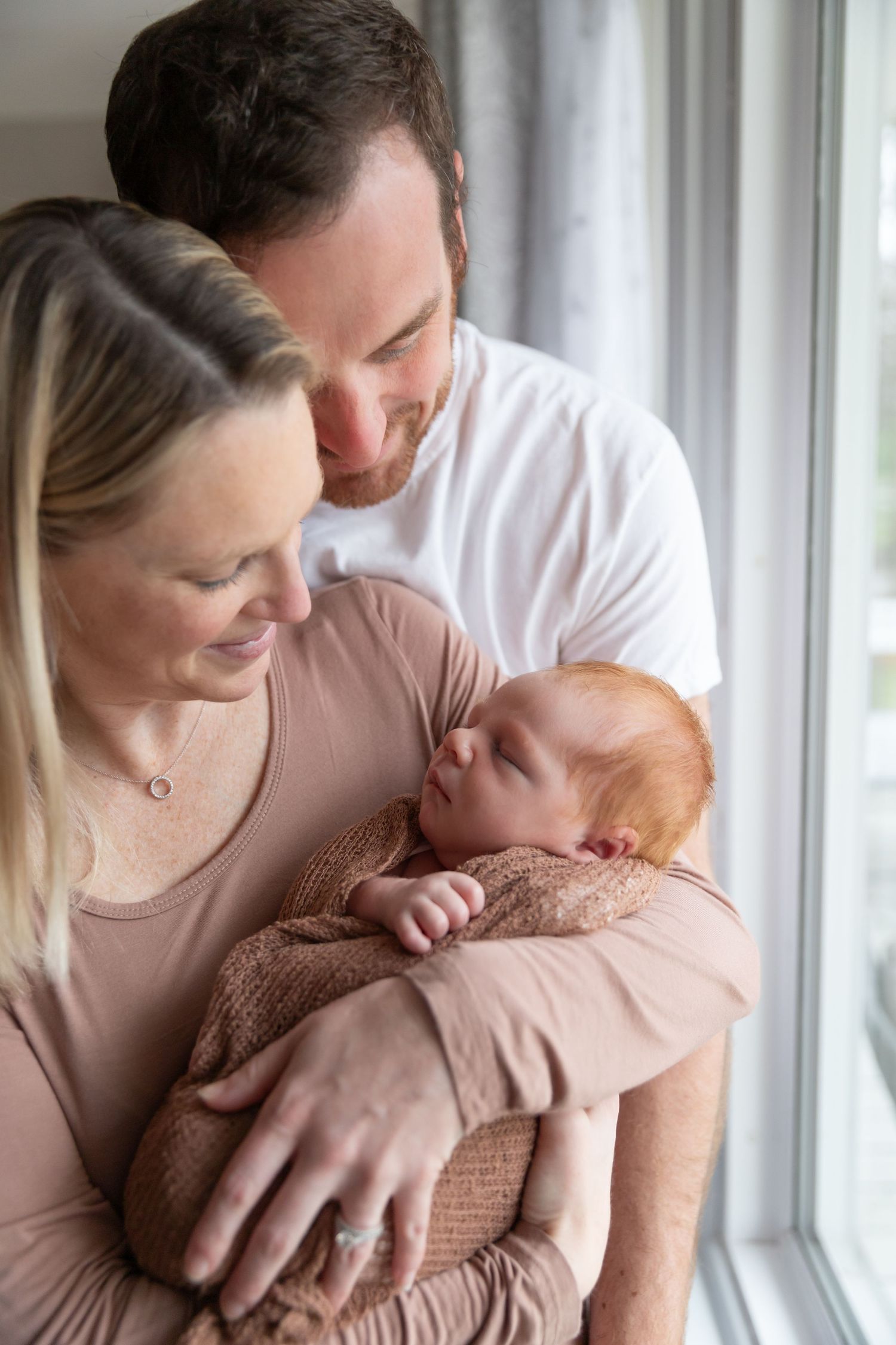 Tender moments between parents and newborn by window in natural light.
