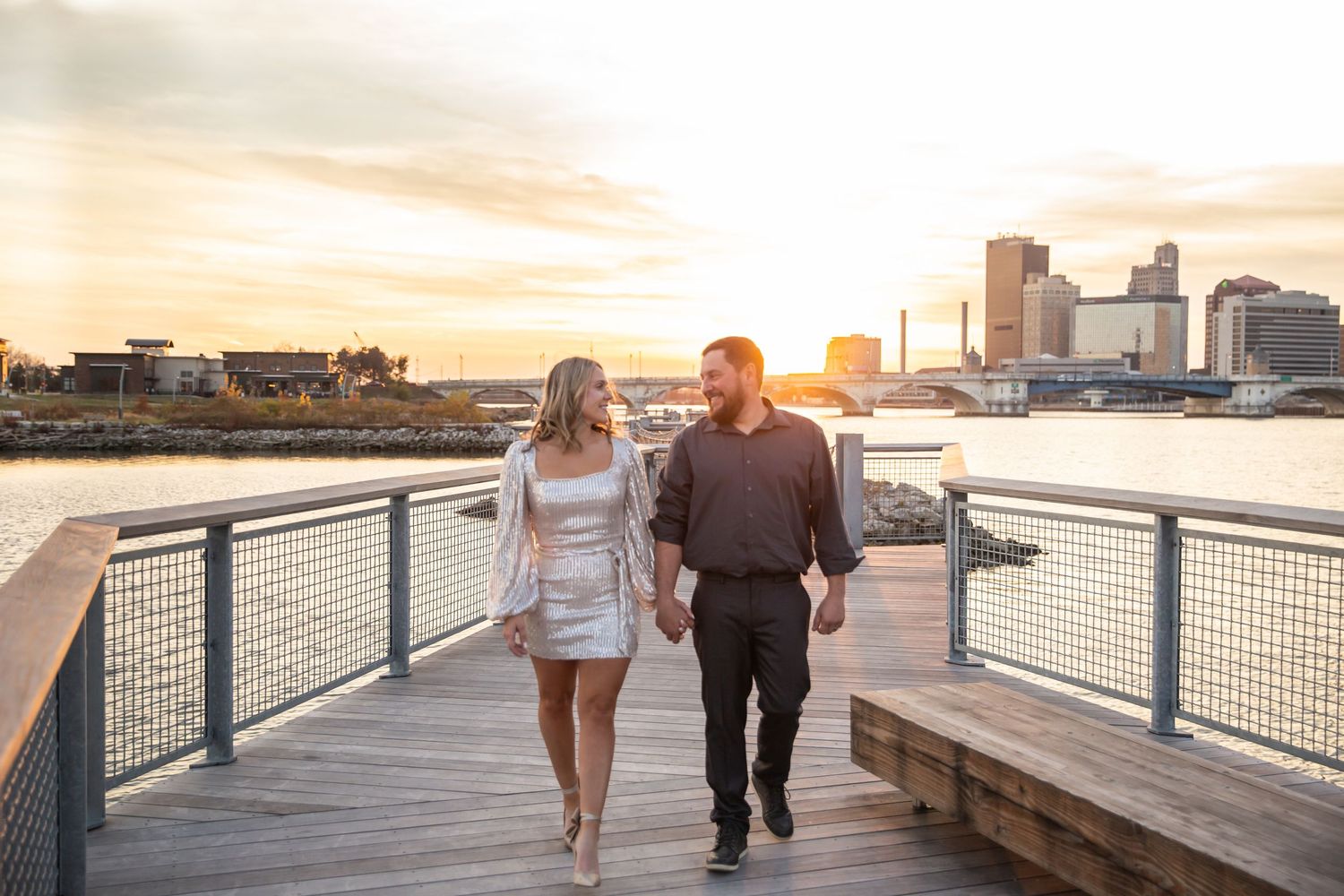 Couple walking along urban riverside boardwalk during golden hour sunset.