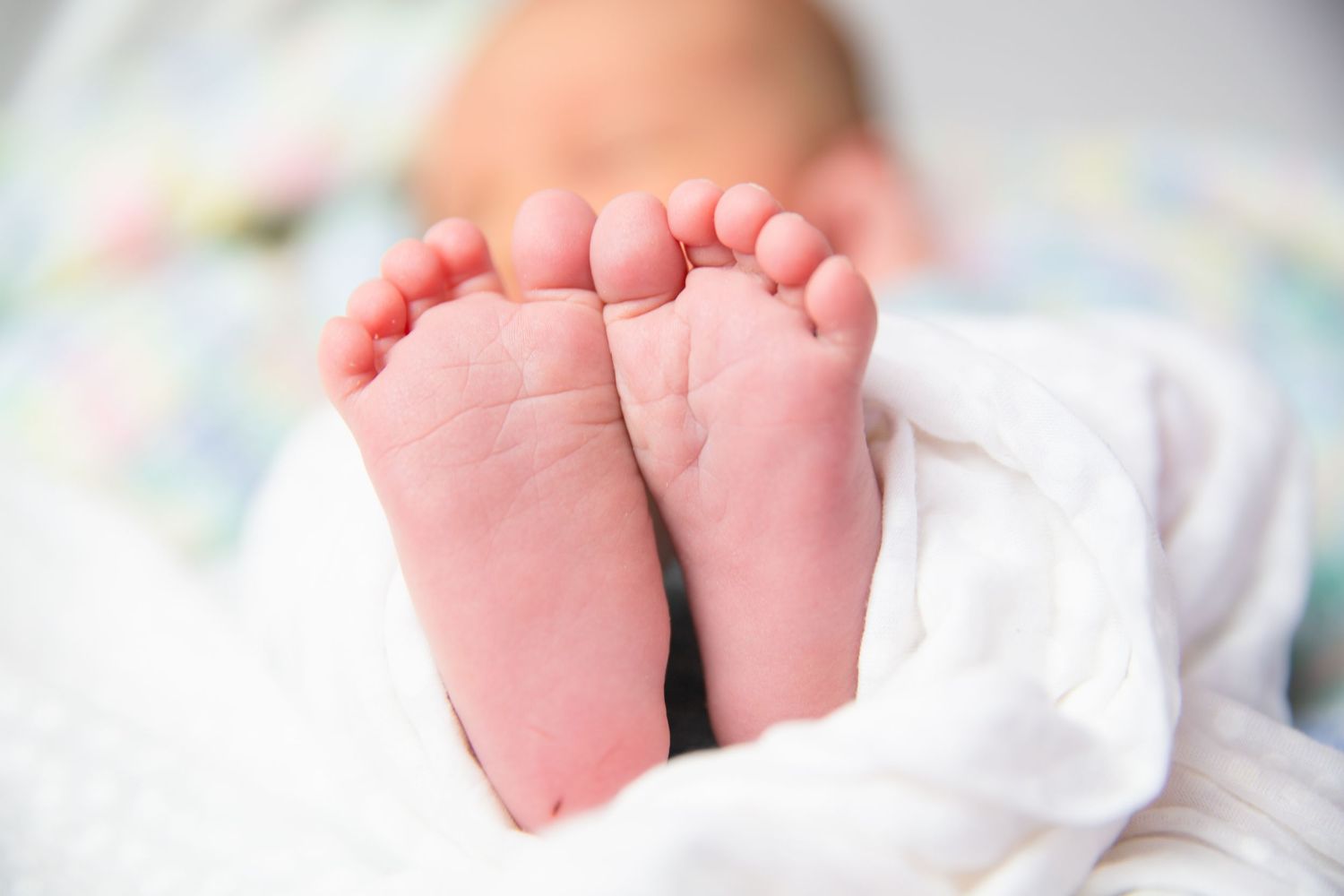 Close-up series of tiny newborn baby feet wrapped in white fabric.
