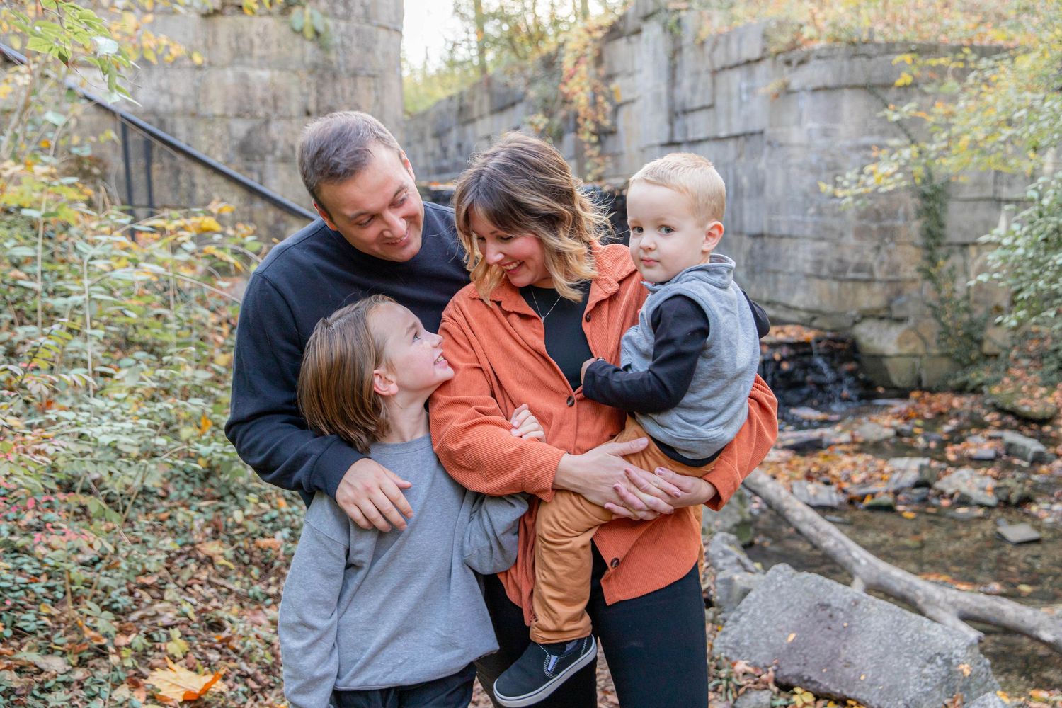 Family shares joyful embrace during autumn photoshoot among stone ruins.