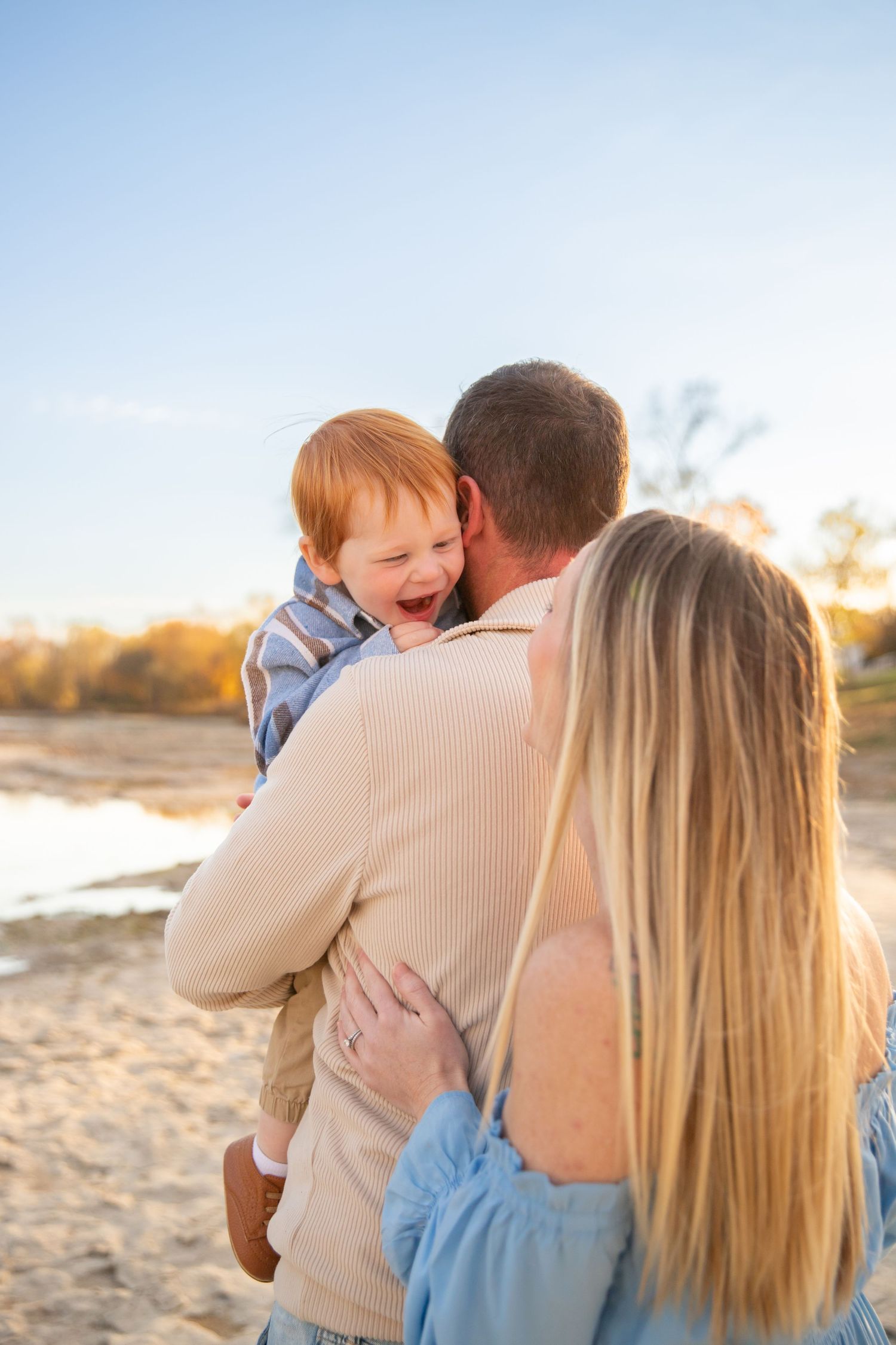 A family embraces together on a sandy beach during golden hour sunset, creating a warm and intimate moment.