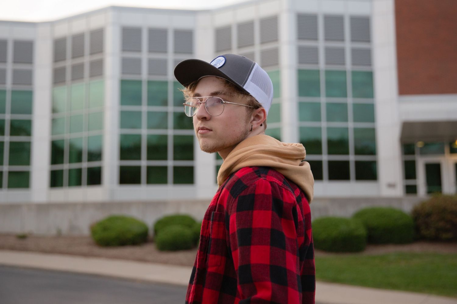 Person in red buffalo plaid flannel and baseball cap stands outside modern building.