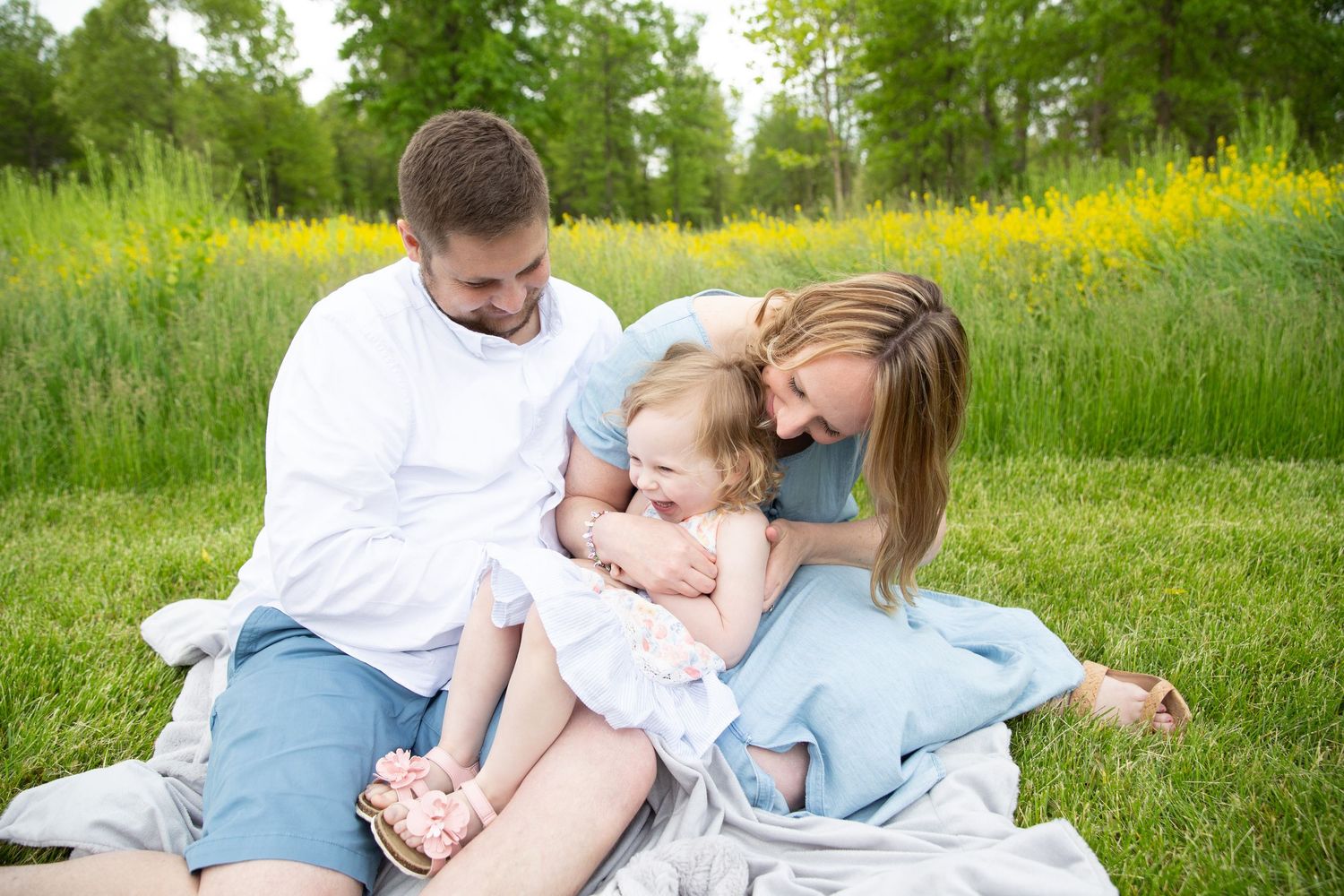 Family enjoying a tender moment together on a blanket in a lush green field.