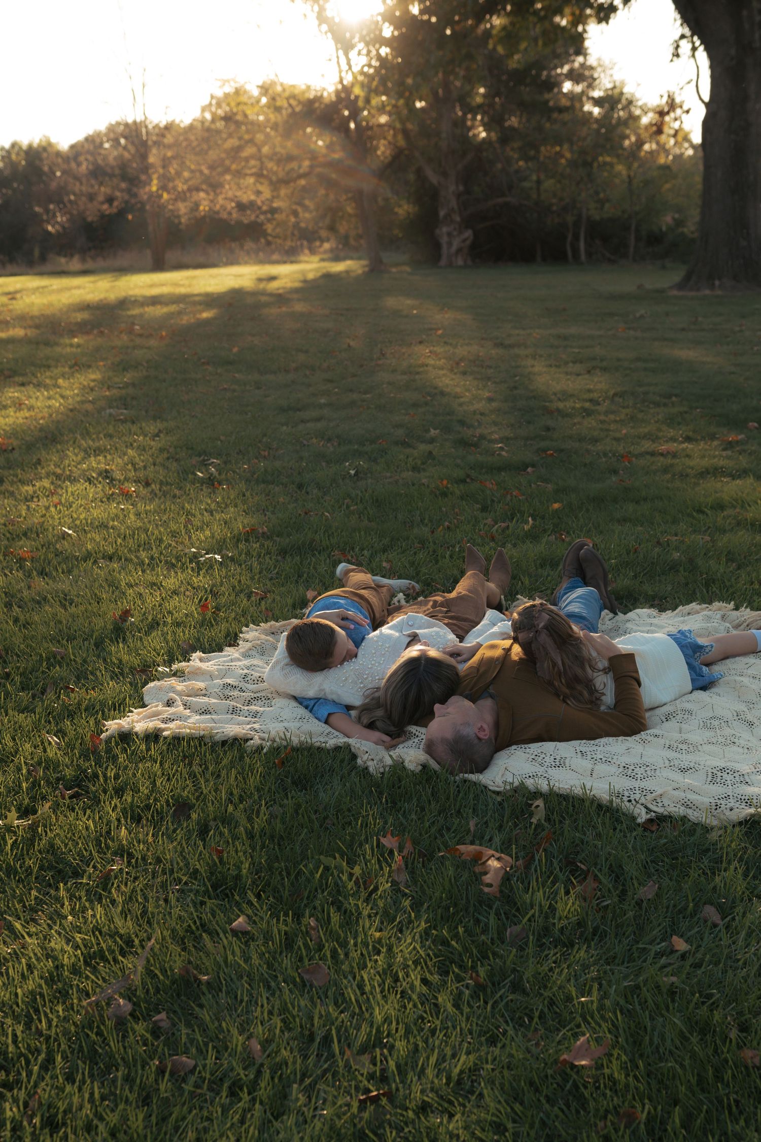 Family lying on a blanket in a sunny park during golden hour, enjoying a peaceful outdoor moment together.
