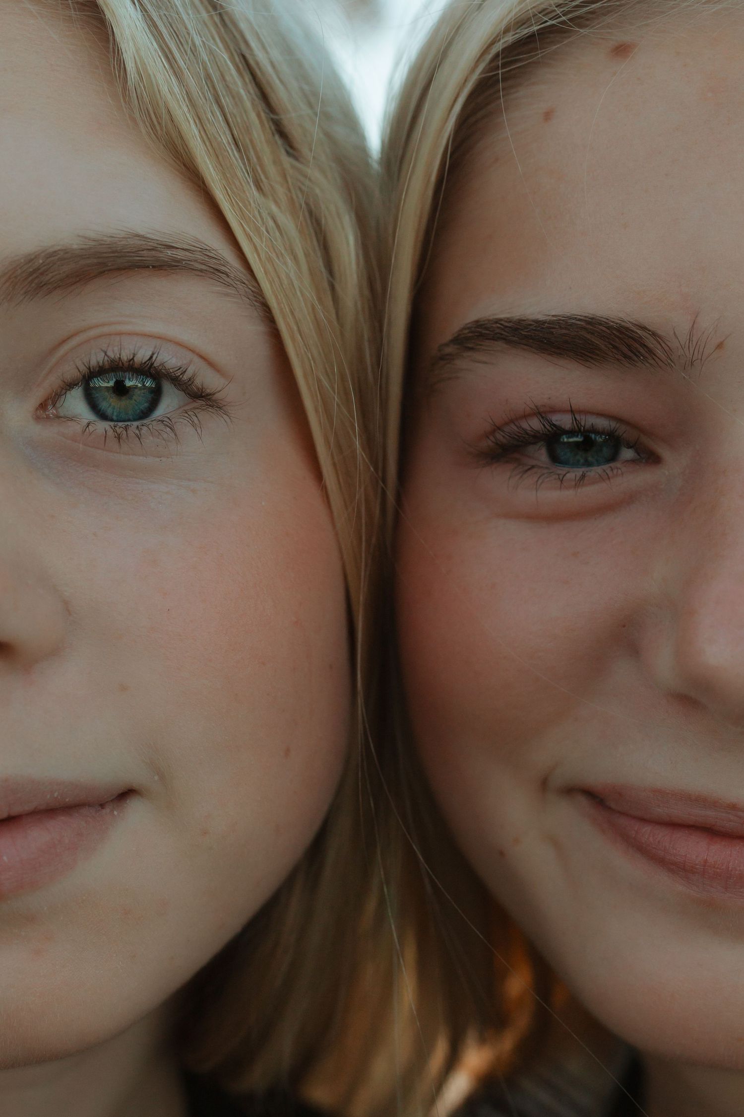 Close-up portrait of two young blonde women with blue eyes pressing their faces together and smiling.