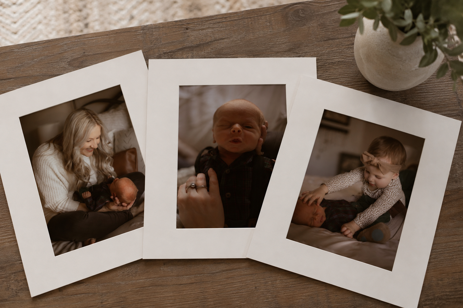 Three printed family photos on wood surface showing a mother with newborn, baby portrait, and toddler with pumpkin.