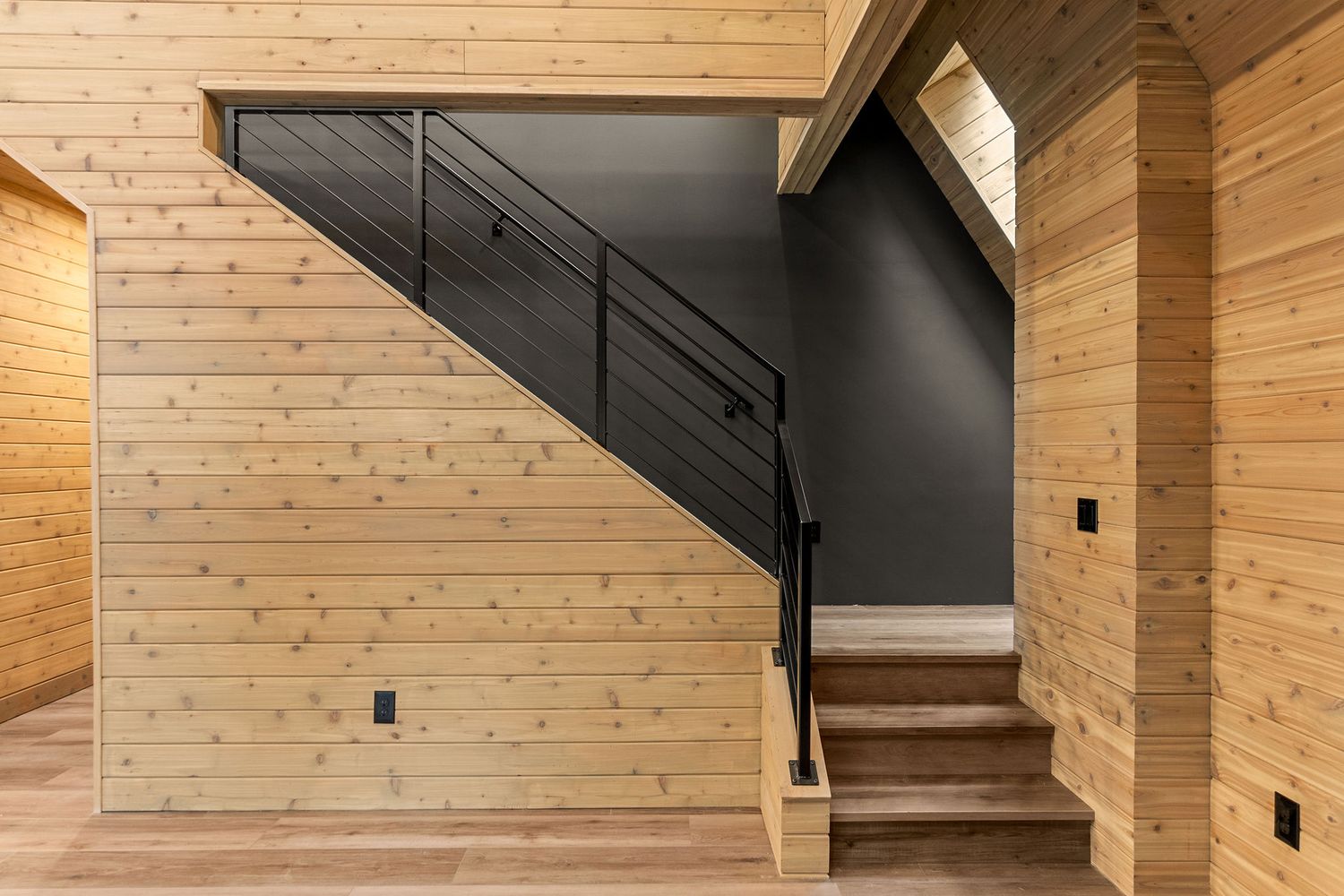 Modern staircase with black railings and natural wood paneling in contemporary home interior.