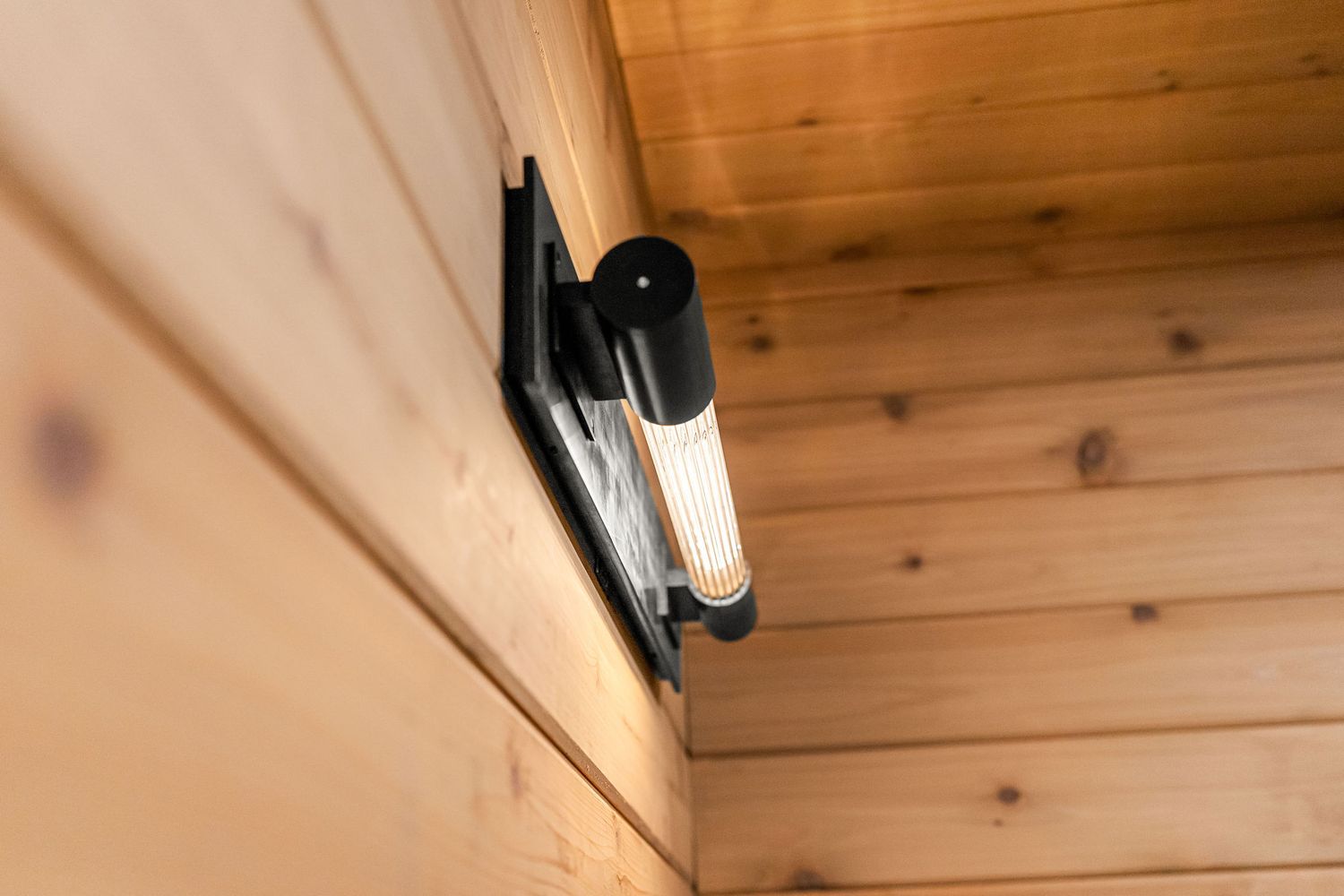 Modern matte black bathroom faucet mounted on dark granite countertop against wood paneled wall.