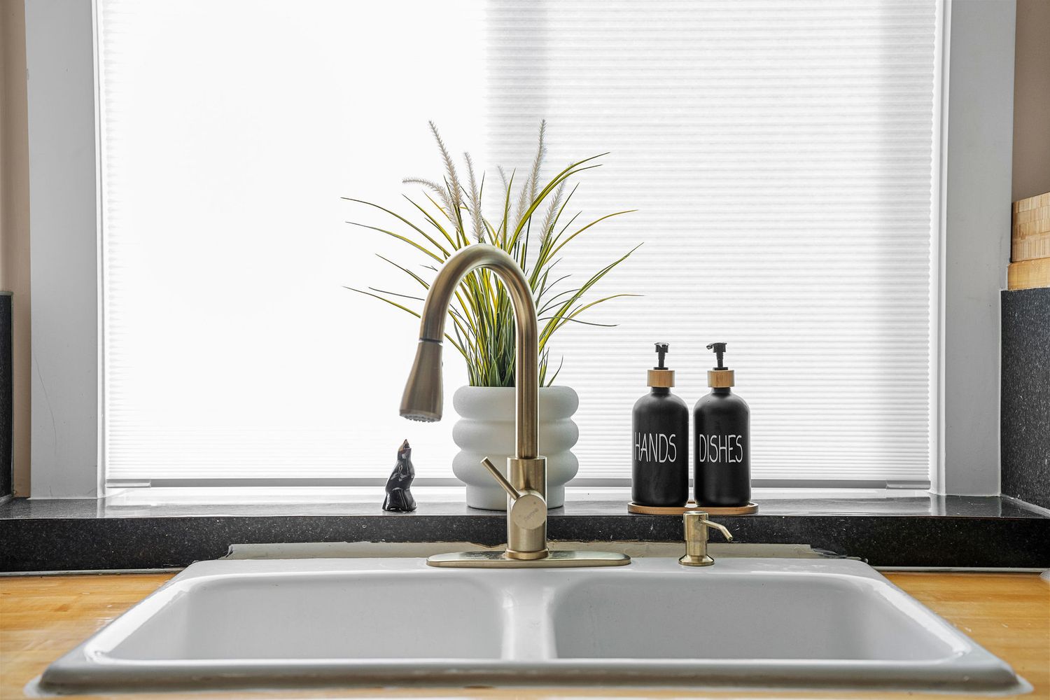 Clean modern kitchen counter with white sink and minimal decor under large window.
