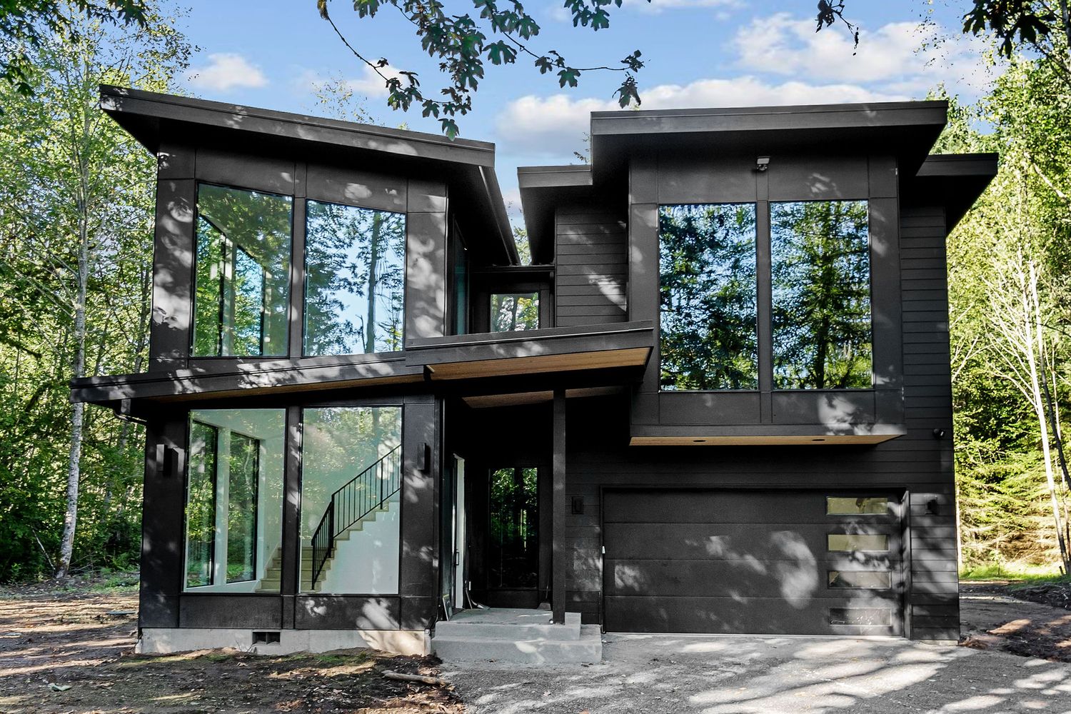 Black modern house exterior with large windows nestled among lush green forest setting.