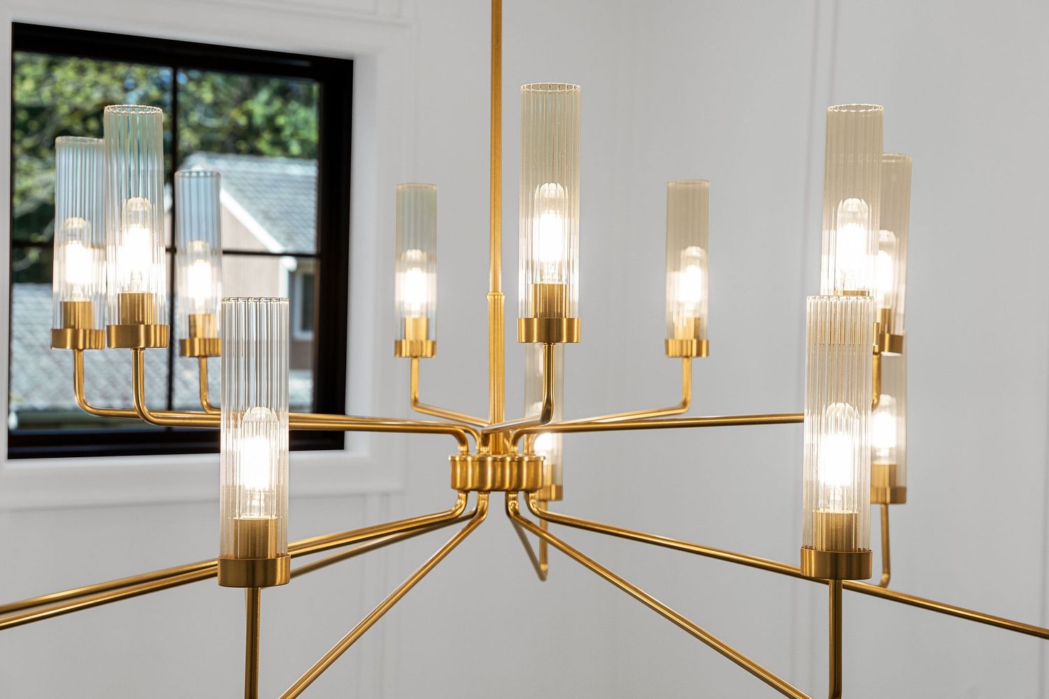 Modern brass chandelier with linear arms and glass cylinder shades illuminates a contemporary interior space.