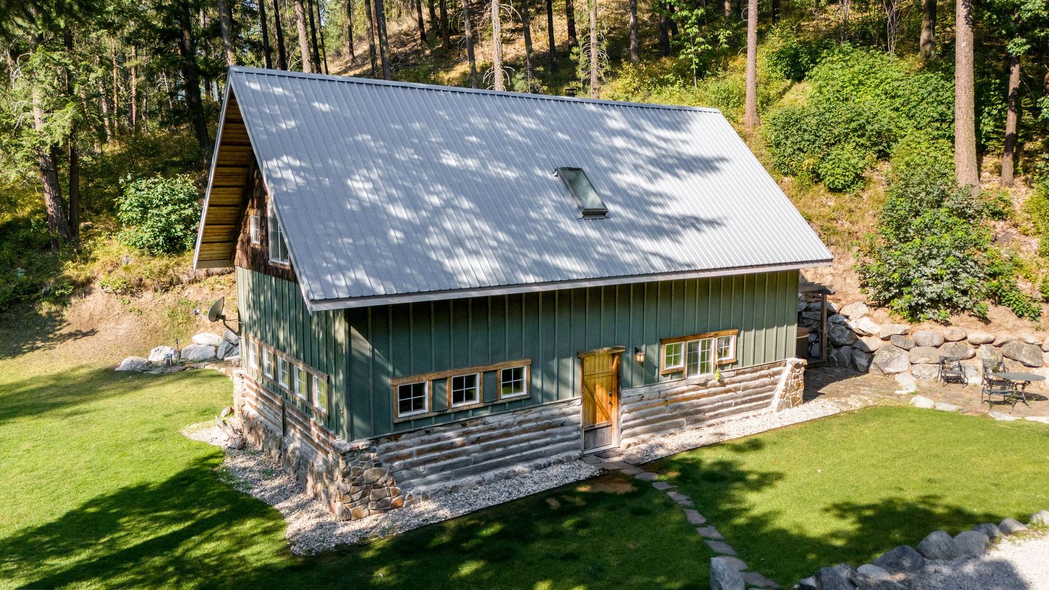 Aerial view of rustic mountain cabin with metal roof nestled in a wooded setting.