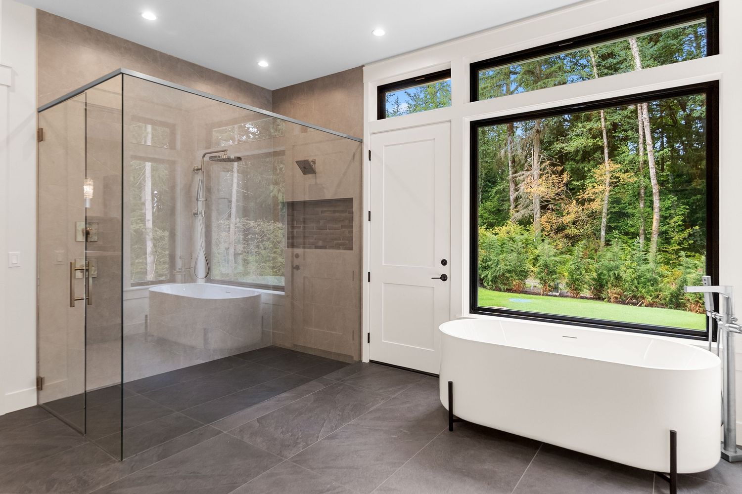 Modern bathroom featuring a frameless glass shower enclosure and large window overlooking green trees.