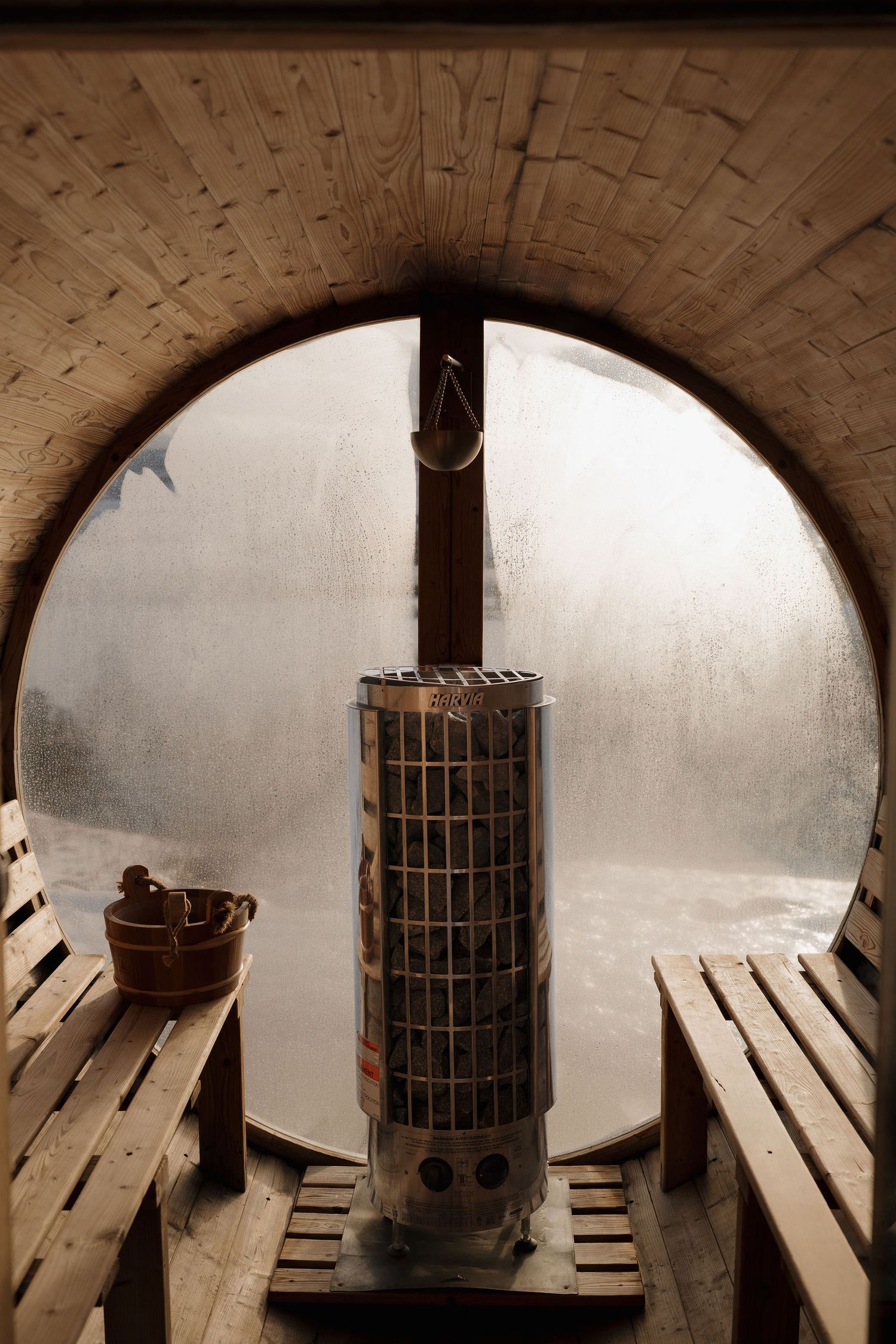 A dark underground prison cell with wooden benches and a metal heating stove in the center beneath an arched ceiling.