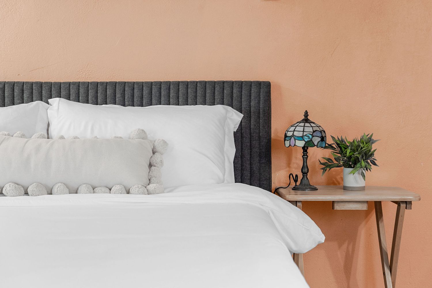 Contemporary bedroom design with plush white bedding and coral colored accent wall.