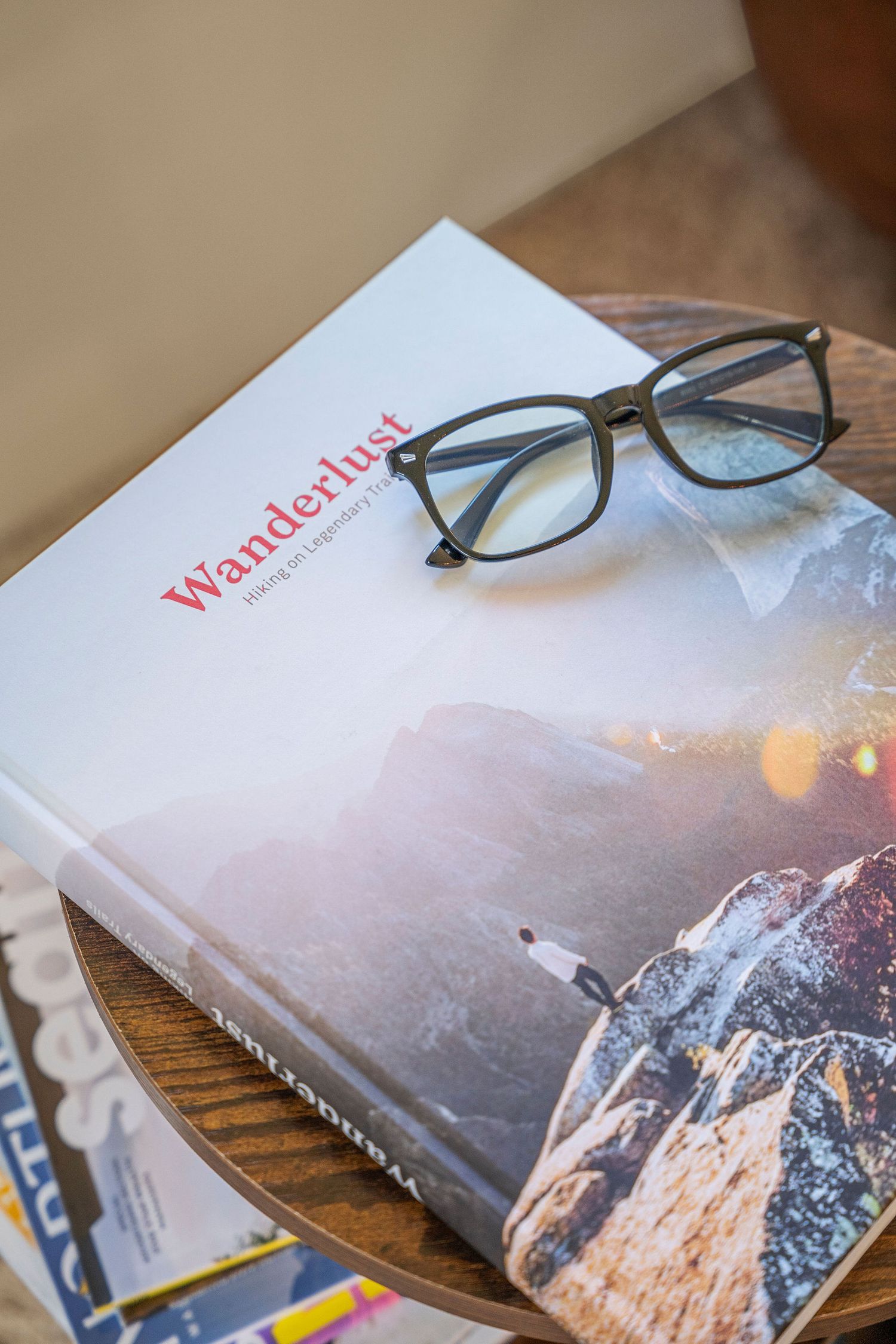 Coffee table book with mountain landscape cover and reading glasses placed on wooden surface.