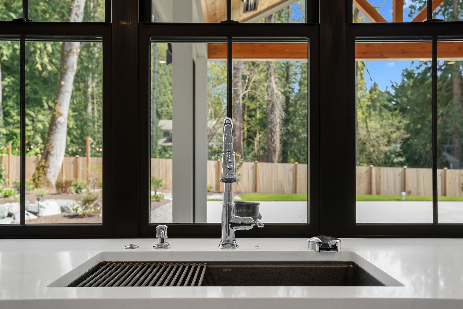 Modern kitchen design features a sleek stainless steel sink with large windows showcasing lush greenery outside.