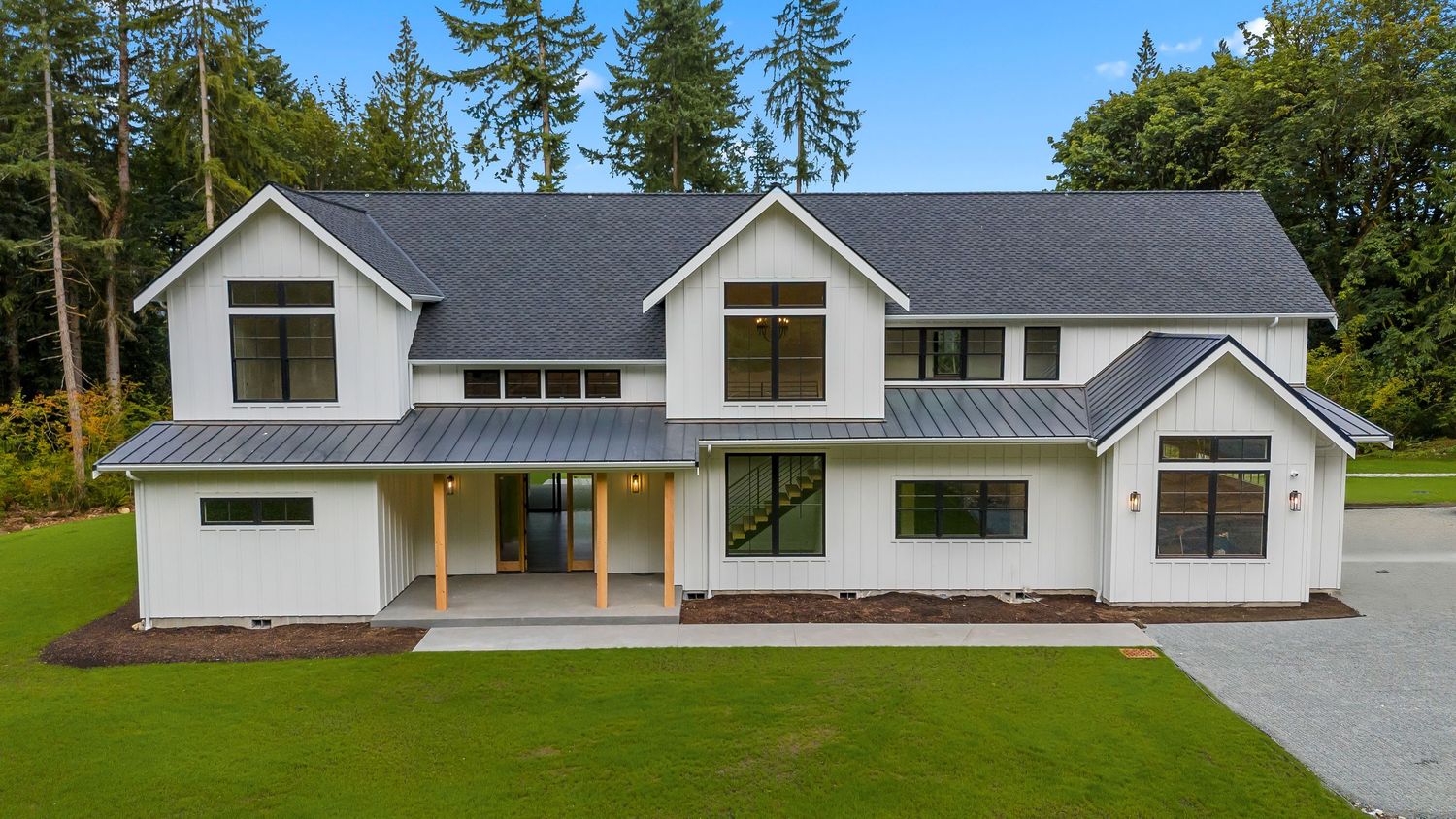 Contemporary farmhouse exterior with metal roof accents and large windows surrounded by evergreens.