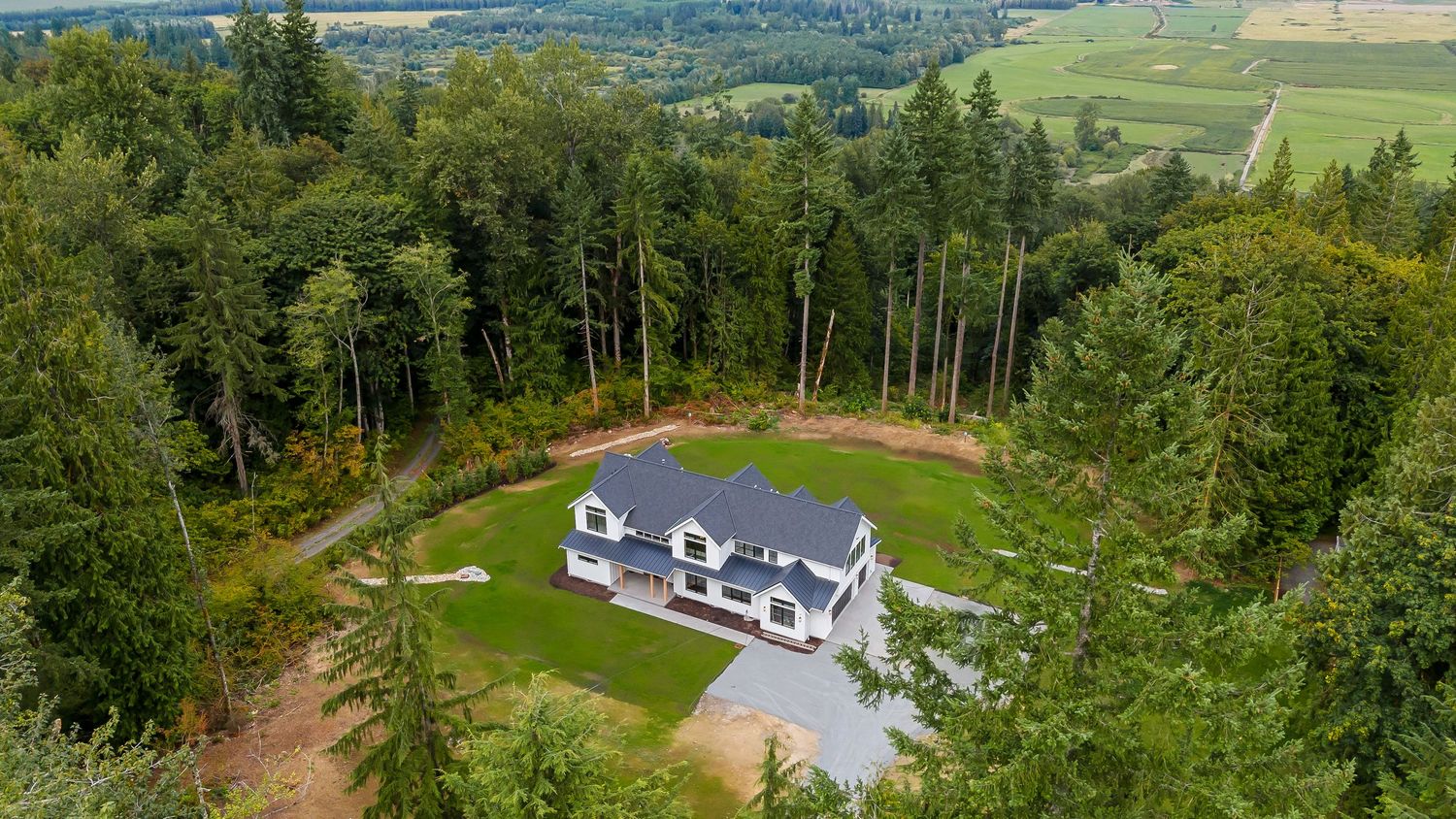 Panoramic aerial view of a modern house property surrounded by green lawns and forest.