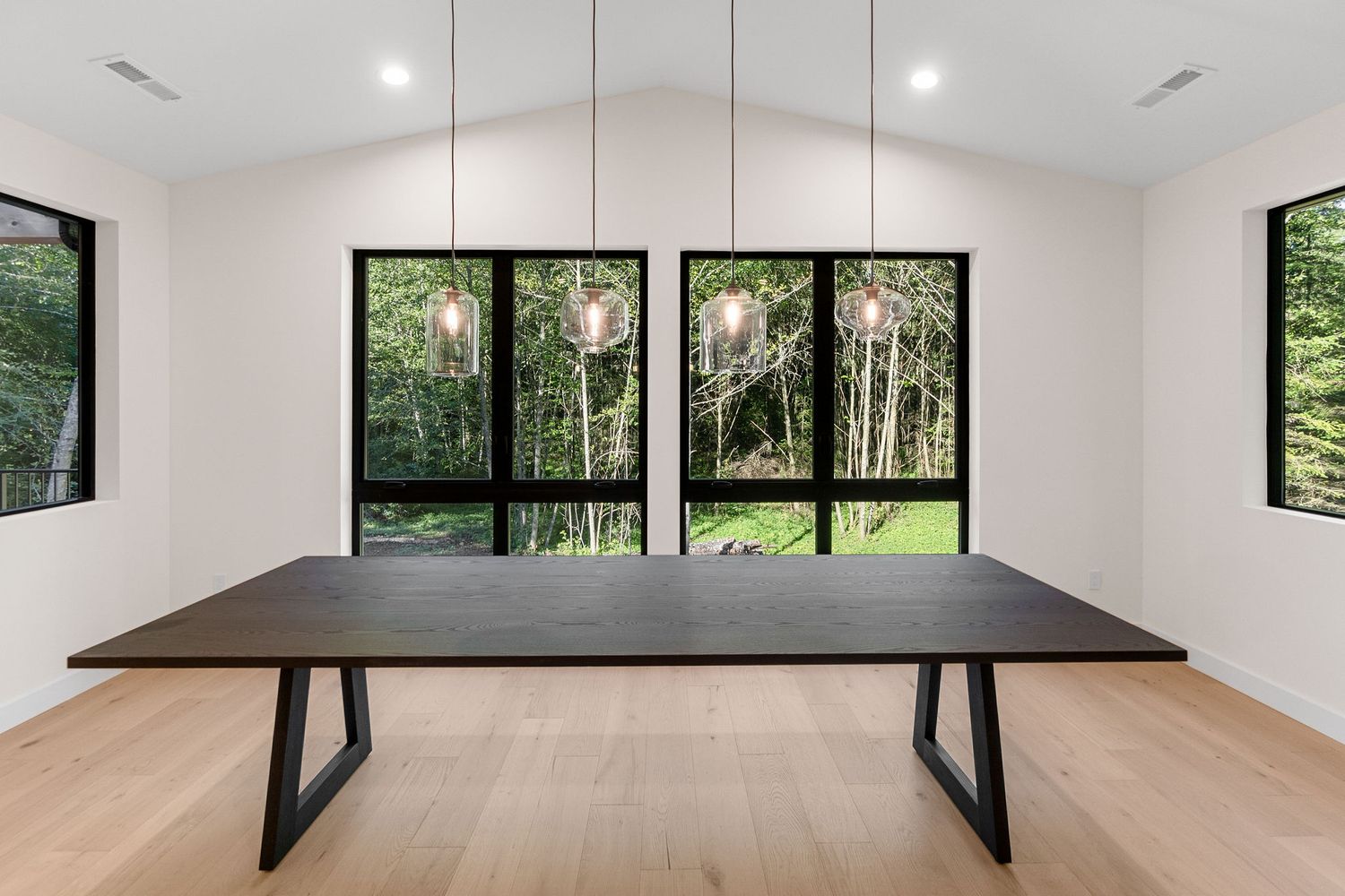 Open concept living area with vaulted ceiling and large windows showcasing forest views.