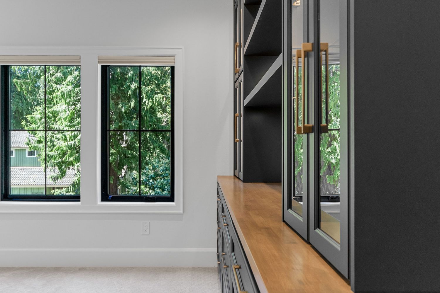 Contemporary kitchen with white walls, black cabinets, and large windows offering forest views.