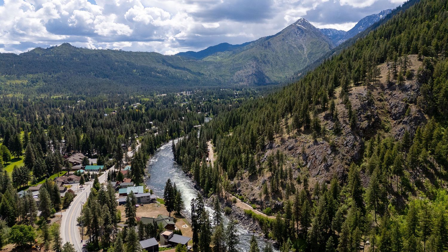 Panoramic mountain landscape with evergreen forests and dramatic cloudy skies.