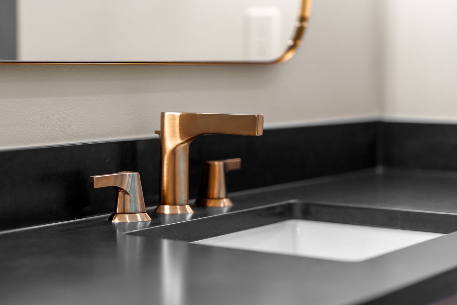 Modern brass bathroom faucet with matte black countertop and white undermount sink.