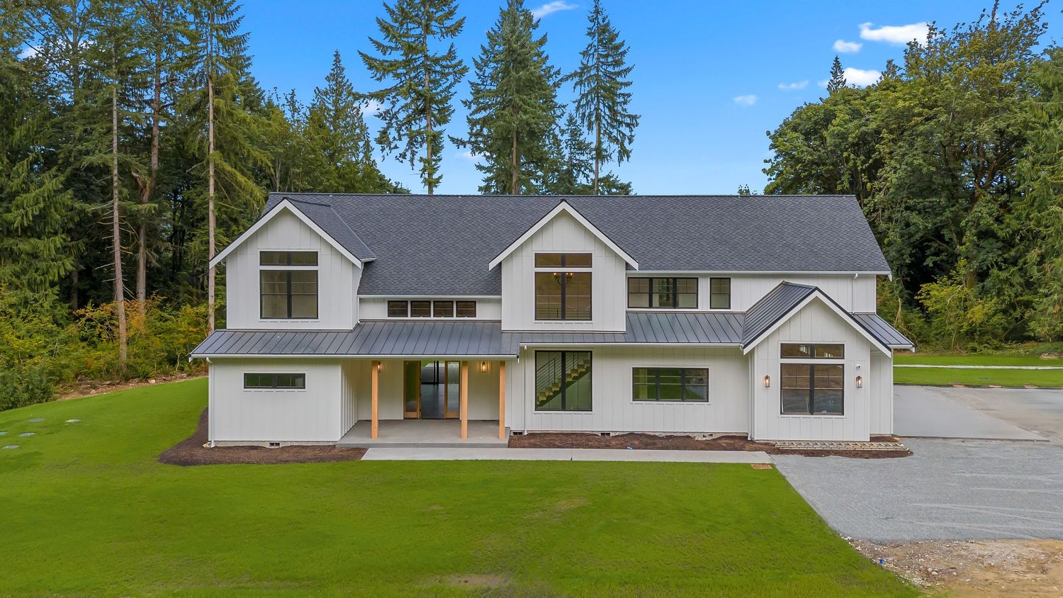 Row of modern residential houses with grey roofs set against a backdrop of evergreen trees.