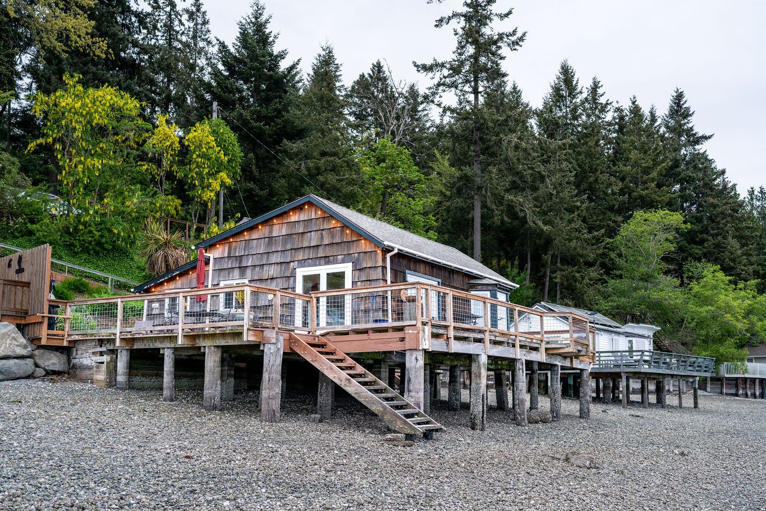 Beachfront cabins nestled among evergreen trees along a rocky shoreline with mountain views in the distance.