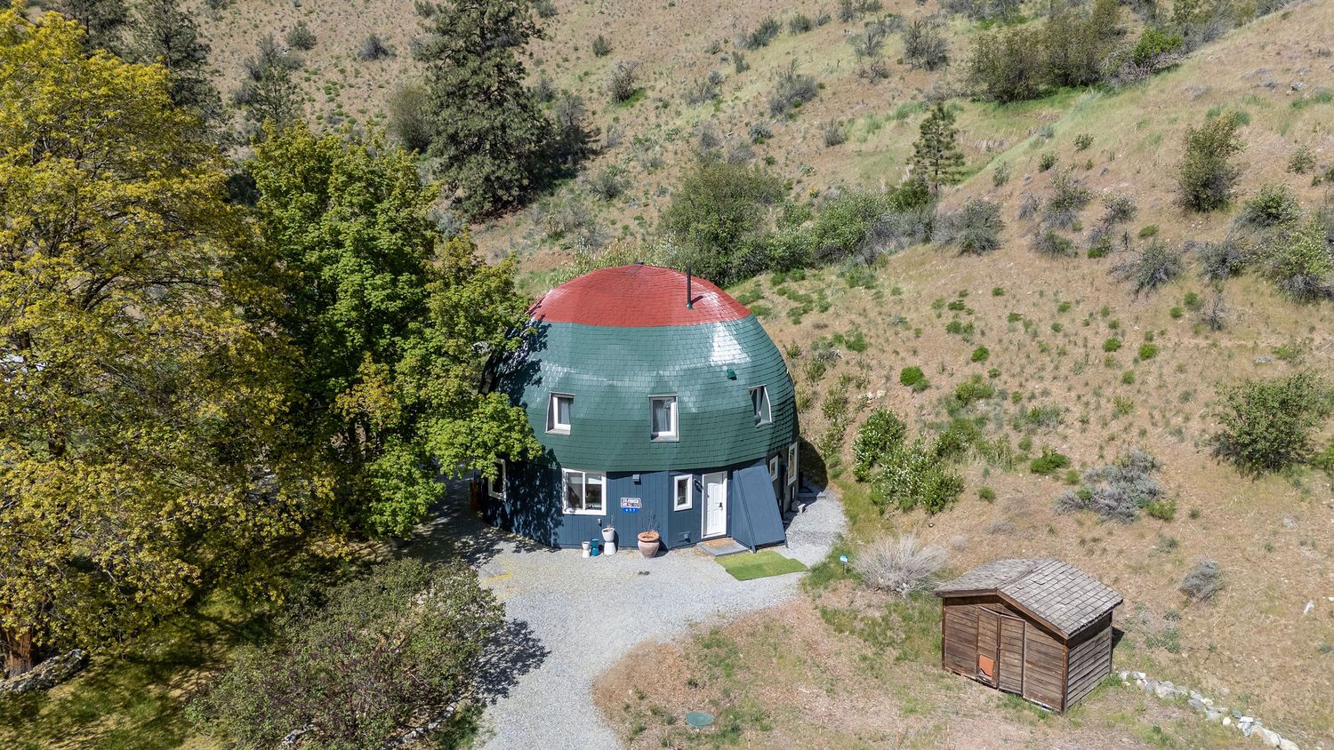Aerial drone view of modern homes nestled among evergreen trees on a hillside property.