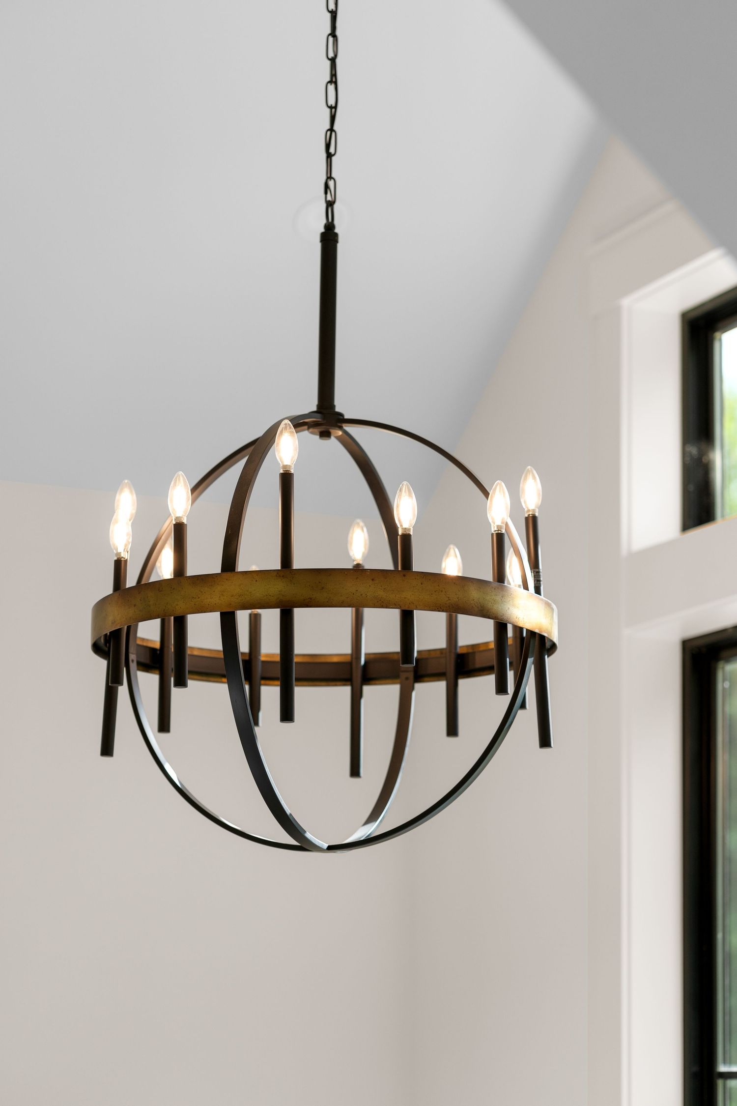 Elegant black metal chandelier with circular design hanging from vaulted white ceiling.