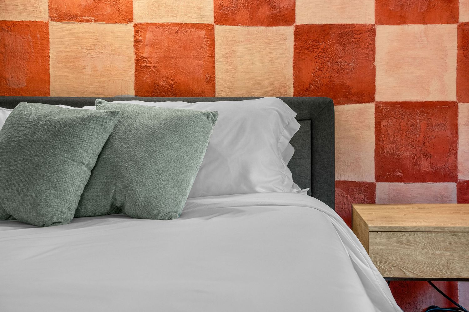 Modern bedroom interior with red and white checkered accent wall and sage green throw pillows.
